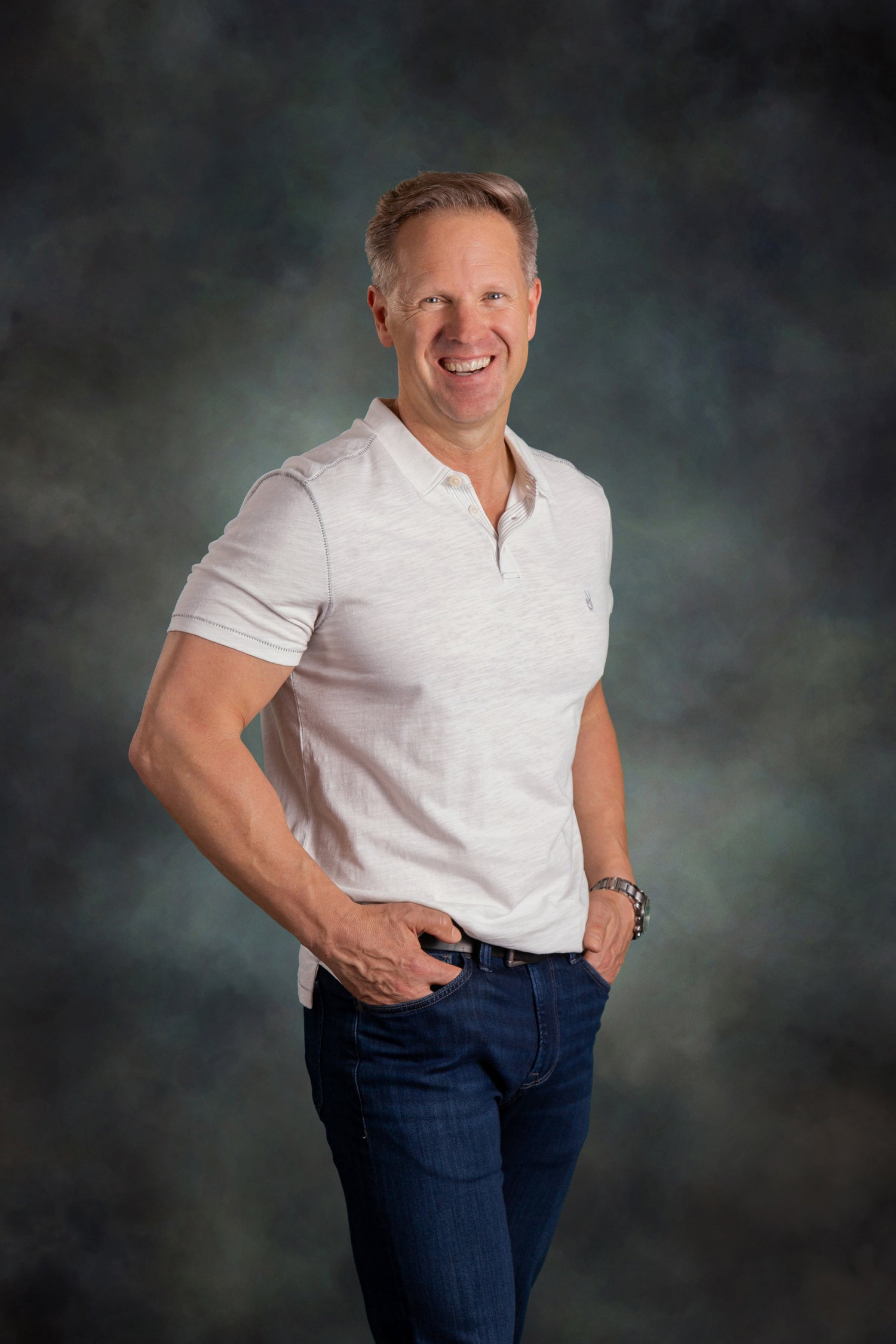 Man wearing a light gray polo shirt and dark blue jeans against a dark background